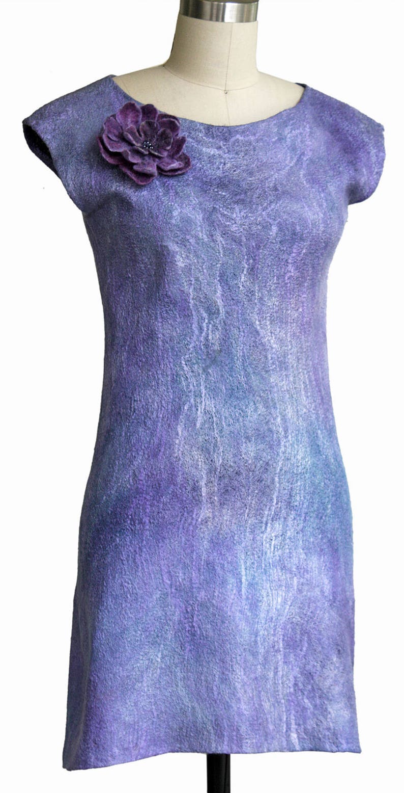 May include: A purple dress with a flower embellishment on the bodice. The dress has a scoop neck and short sleeves. The fabric has a textured, marbled look.