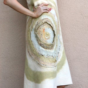 May include: A woman wearing a white dress with a circular pattern in shades of beige, brown, and gold. The dress has a flowing, asymmetrical hemline. She is wearing nude heels.