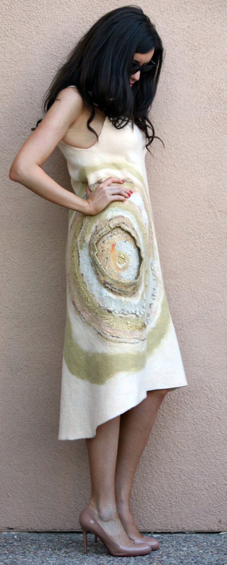 May include: A woman wearing a white dress with a circular pattern in shades of beige, brown, and gold. The dress has a flowing, asymmetrical hemline. She is wearing nude heels.