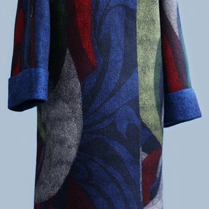 May include: A long, patterned coat with a blue, red, green, and gray design. The coat features a textured blue collar and cuffs. The coat is displayed on a mannequin.