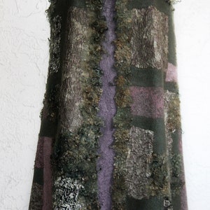 May include: A sleeveless, handcrafted vest in earthy tones. The vest features a patchwork design with shades of green, purple, and brown. The textured wool fabric is accented with a decorative button closure. The garment is displayed on a mannequin.