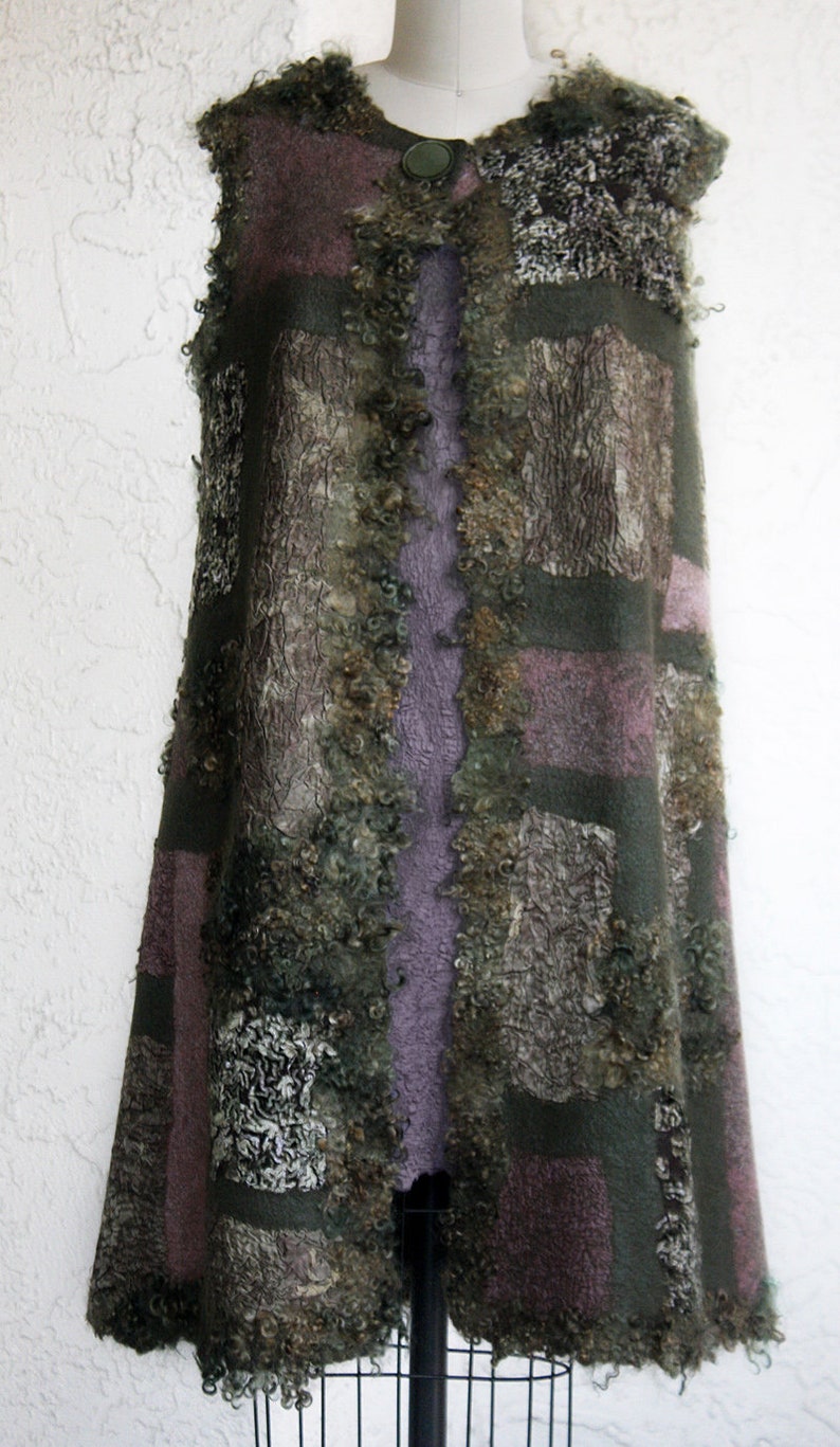 May include: A sleeveless, handcrafted vest in earthy tones. The vest features a patchwork design with shades of green, purple, and brown. The textured wool fabric is accented with a decorative button closure. The garment is displayed on a mannequin.