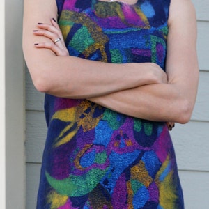 May include: A woman wearing a sleeveless dress with a colorful abstract pattern. The dress is blue with splashes of yellow, green, pink, and purple.
