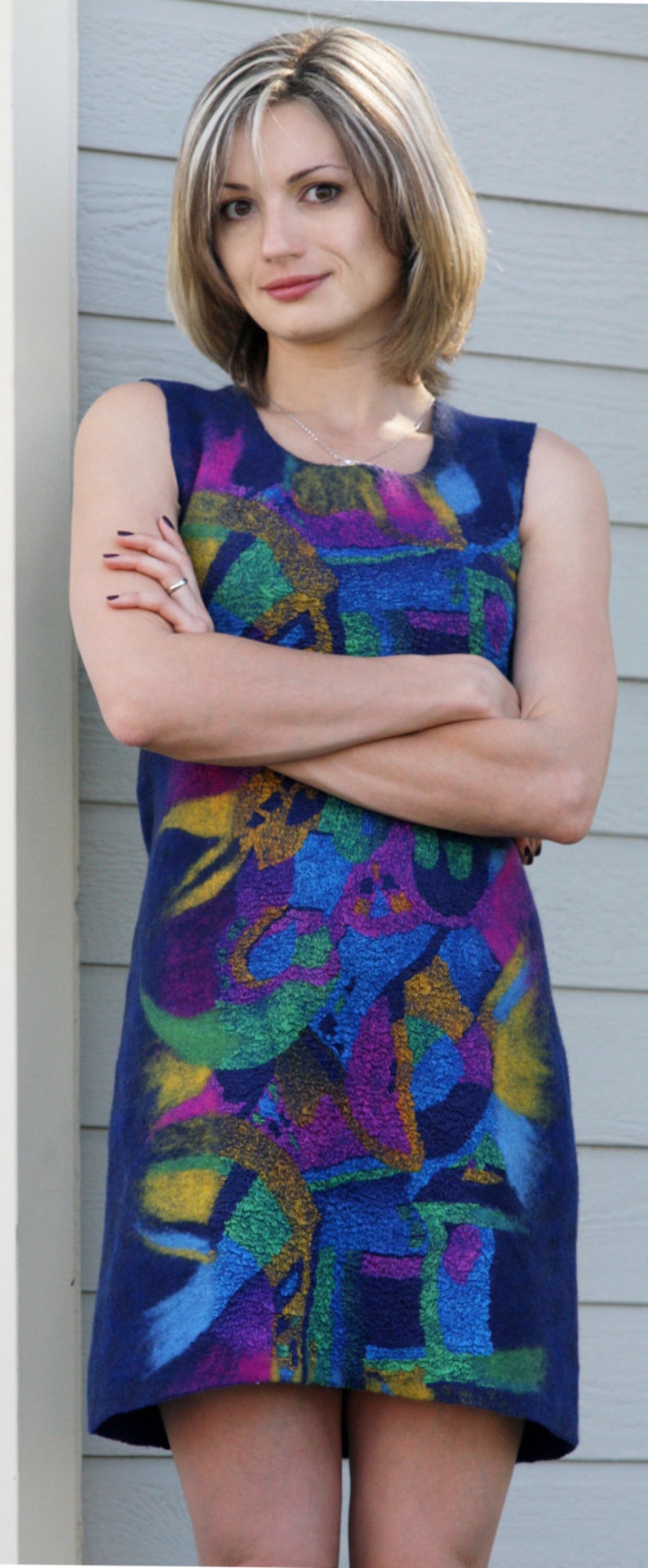 May include: A woman wearing a sleeveless dress with a colorful abstract pattern. The dress is blue with splashes of yellow, green, pink, and purple.