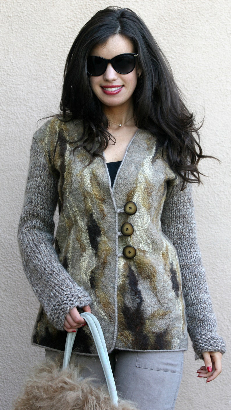 May include: A woman wearing a long-sleeved, button-down jacket with a unique pattern in shades of brown, gray, and gold. The jacket has large, round buttons and is paired with gray pants. She is also wearing sunglasses.
