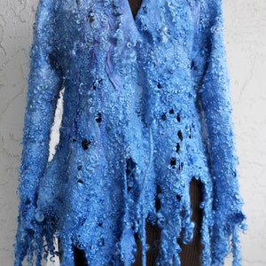 May include: A light blue, felted wool jacket with a unique, textured appearance. The jacket features a V-neck and long sleeves, with a fringed hemline. The wool has a curly, almost cloud-like texture, and the jacket is displayed on a mannequin.