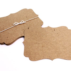 May include: A stack of brown, scalloped-edge paper tags with a white string tied around them. The tags are blank and ready for writing.