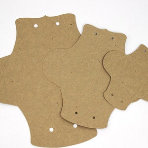 Puede incluir: Tres compresas menstruales de cart&oacute;n marr&oacute;n de diferentes tama&ntilde;os. Las compresas tienen agujeros perforados.