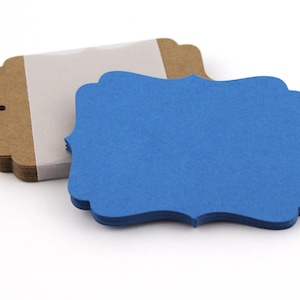 May include: A stack of brown kraft paper gift tags with scalloped edges and a hole for string. The tags are topped with a single blue tag with scalloped edges.