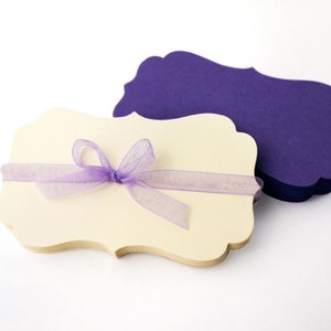 May include: A stack of ivory-colored, scalloped-edge note cards with a lavender ribbon tied in a bow. The note cards are stacked on top of a stack of purple, scalloped-edge note cards.