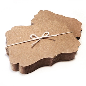 May include: A stack of brown kraft paper gift tags with scalloped edges, tied together with a white twine bow.