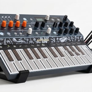 May include: A dark gray synthesizer with a keyboard and multiple knobs and buttons. The synthesizer has a black stand and is connected to other audio equipment with cables. The word "ARTURIA" is printed on the synthesizer.