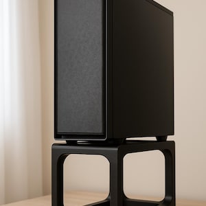 Puede incluir: Una caja de ordenador negra con un panel frontal texturizado se asienta sobre un soporte negro a juego. El soporte tiene un diseño cuadrado y abierto. La configuración está sobre una superficie de madera clara, con un fondo neutro.