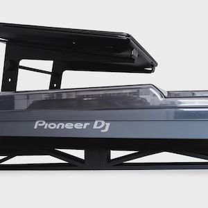 Może przedstawiać: Szary kontroler Pioneer DJ z czarnym stojakiem i czarnym blatem. Kontroler ma przezroczystą plastikową osłonę i logo Pioneer DJ w kolorze białym. Stojak jest wykonany z czarnego metalu.