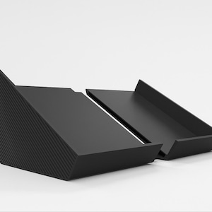 May include: Two matte black, angled trays. One tray has a textured, diagonal pattern on its side. The trays are positioned on a white surface, with a minimalist design.