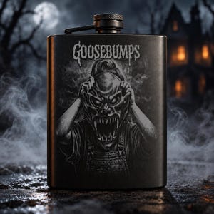May include: A matte black metal flask featuring a graphic illustration of a creature pulling off a mask, with the text GOOSEBUMPS printed in a stylised font above the figure. The flask has a screw-top cap with a hinged arm attached to the top.