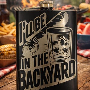 Puede incluir: Petaca negra con tapón de rosca dorado. La petaca presenta un gráfico de un cigarro y un vaso de whisky con cubitos de hielo, y el texto "I'll be in the backyard."