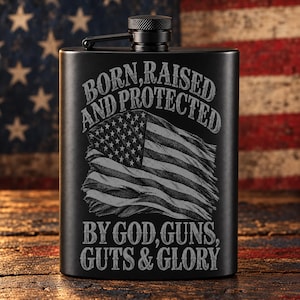 May include: A matte black metal flask featuring an engraved design of a distressed American flag. The text BORN, RAISED AND PROTECTED BY GOD, GUNS, GUTS & GLORY is etched in a bold, weathered font above and below the flag graphic.