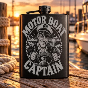 May include: A matte black metal flask featuring a circular engraved graphic of a winking captain at a ship's wheel with a pipe in their mouth. The text MOTOR BOAT CAPTAIN is arched around the central illustration, which includes a rope border.