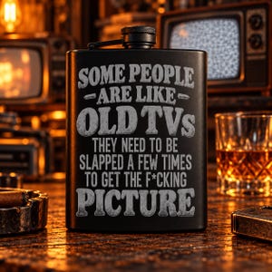 May include: A matte black metal flask featuring the engraved text: SOME PEOPLE ARE LIKE OLD TVs THEY NEED TO BE SLAPPED A FEW TIMES TO GET THE F*CKING PICTURE. The flask has a screw-top cap with a textured grip and a hinged metal arm attachment.