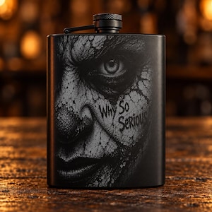 May include: A matte black metal flask featuring a detailed, high-contrast grey graphic of a face with cracked skin texture. The text Why So Serious is printed in a stylised, dripping font on the right side. It has a screw-top cap with a hinged arm.