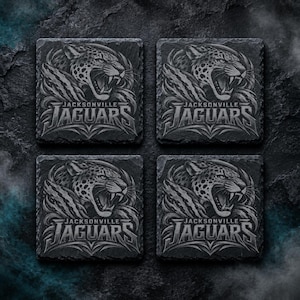 May include: A set of four square slate coasters, each featuring a detailed, engraved graphic of a roaring jaguar head above the text Jacksonville Jaguars. The coasters have a dark, textured stone finish with a monochromatic gray color scheme.
