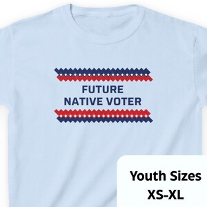 May include: Light blue t-shirt with the text "FUTURE NATIVE VOTER" in white. The text is between two rows of red and blue zig-zag patterns. The shirt is available in youth sizes XS-XL.