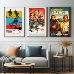 Puede incluir: Se exhiben tres carteles enmarcados de la película "Once Upon a Time in Hollywood". Los carteles presentan imágenes de las estrellas de la película y el título de la película. Los carteles están en marcos negros y cuelgan sobre un sofá gris y mesas de centro de madera.