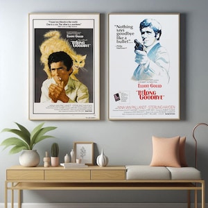 Pode incluir: Dois cartazes de filmes emoldurados de "The Long Goodbye" são exibidos. Um apresenta um homem com um gato, o outro um homem segurando uma arma. Ambos os cartazes têm texto e estão em molduras douradas, montados em uma parede cinza claro.