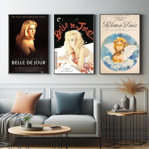 Puede incluir: Tres carteles de películas enmarcados. El primero es un póster oscuro con el texto "BELLE DE JOUR" y el nombre "CATHERINE DENEUVE". El segundo póster tiene el título "BELLE DE JOUR" en rojo y el tercer póster tiene un ángel con un reloj.