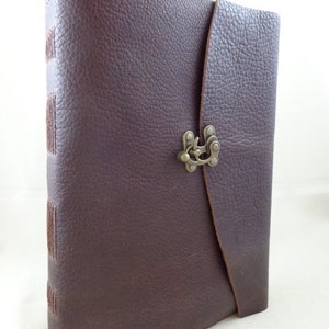 May include: A dark brown leather-bound journal with a flap closure and a metal clasp. The journal has stitching along the spine and a textured leather cover.