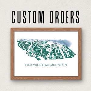 May include: A framed print with a mountain map design in shades of green and white. The text "CUSTOM ORDERS" is above the frame, and "PICK YOUR OWN MOUNTAIN" is below. The frame is a light brown color.