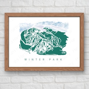 May include: A framed print featuring a green and white illustration of a ski resort map. The artwork includes the text "WINTER PARK" in white letters. The frame is made of light brown wood, and the background is a white brick wall.