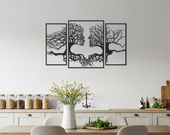 Op de afbeelding: Zwarte metalen wandkunstset met twee gezichten die verweven zijn met boomtakken en wortels. Het kunstwerk is verdeeld in drie ingelijste panelen, wat een unieke en artistieke weergave creëert. Het ontwerp heeft ingewikkelde details en een moderne esthetiek.