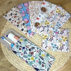 Peut inclure: Plusieurs étuis à brosse à dents en tissu avec différents motifs, dont des imprimés animaliers, des motifs floraux et des personnages de dessins animés. Un étui contient une brosse à dents et du dentifrice. Les étuis sont disposés sur un tapis tissé.