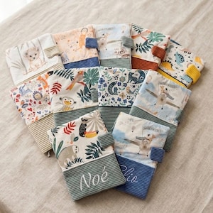 Peut inclure: Une collection de housses en tissu rectangulaires avec divers imprimés colorés d'animaux et de nature. Chaque housse possède une section inférieure en velours côtelé texturé, certaines avec des prénoms brodés comme Noé et Clio, et une petite patte latérale.