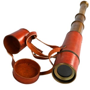 May include: A vintage brass and leather telescope with a red leather casing and a matching leather cap. The telescope has a leather strap and is designed for viewing distant objects. The brass sections are visible.