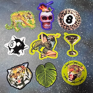 May include: A collection of nine stickers featuring a tiger on green glitter, a skull cocktail, a leopard print eight ball, a spiked eight ball, a person with a leopard, a martini glass, a tiger face, a green leaf, and a leopard in barbed wire.