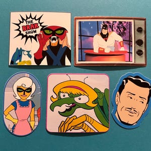 May include: A selection of cartoon character stickers in various shapes. The stickers depict characters from The Brak Show, Space Ghost, and other animated figures. The stickers are rectangular, oval, and square shaped.