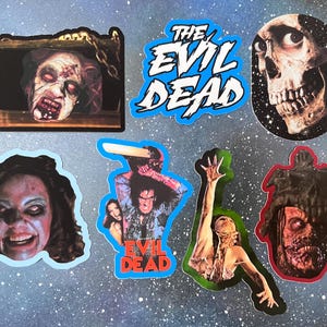 May include: A collection of six stickers featuring imagery from The Evil Dead, including a skull, a character with a chainsaw, a possessed figure, and the movie title text in blue and white, all displayed against a speckled blue background.