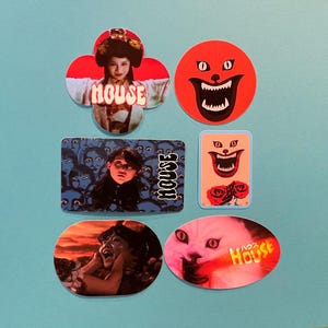 May include: A selection of vibrant stickers inspired by the Japanese horror film "House." The designs include a red clown face, a cat with the word "House" in Japanese, and other film-related graphics. The stickers are displayed on a light blue background.