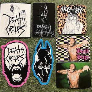 Può includere: Una collezione di adesivi e stampe Death Grips. I disegni includono membri della band, illustrazioni stilizzate e il logo della band in vari colori e sfondi. Gli adesivi presentano disegni in bianco e nero, rosa, blu e stampa leopardata.