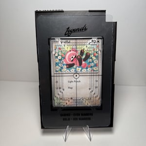May include: A black card holder displaying a trading card. The card features a pink and black cartoon character with the text "Light Punch" and "Flop". The card is surrounded by a floral design and a grid. The card holder has the word "Legends" on it.