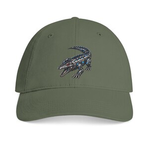 May include: An olive green baseball cap featuring a centered graphic of a mechanical crocodile. The robotic reptile is depicted in shades of metallic silver and blue with glowing red eyes, shown in a crouched position with its mouth slightly open.