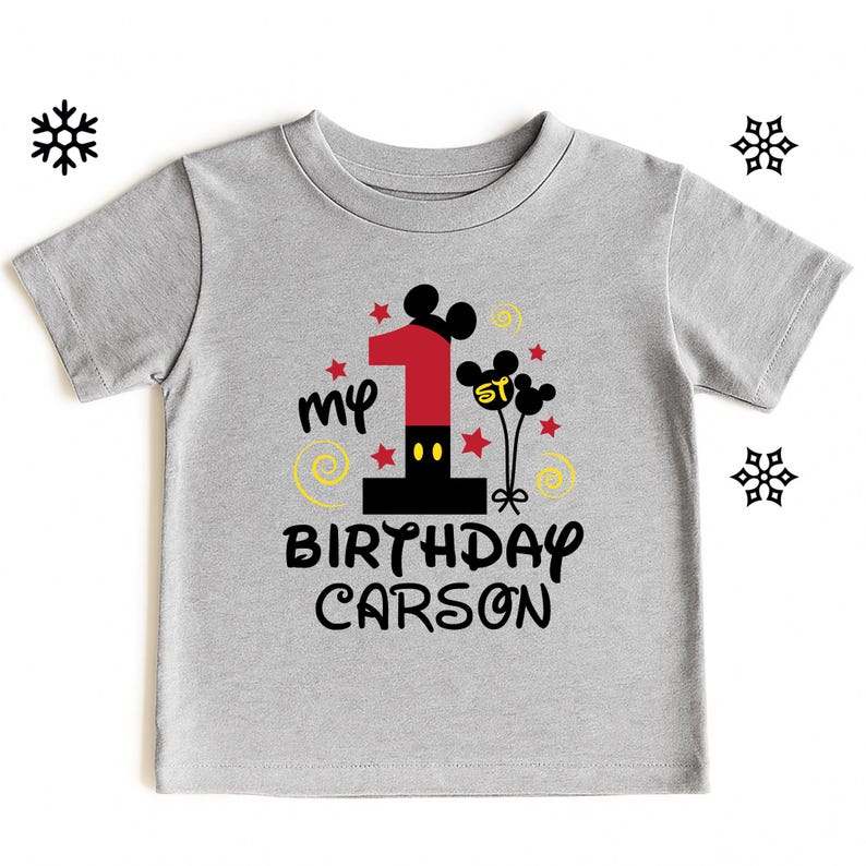 K&ouml;nnte beinhalten: Graues Kurzarm-T-Shirt mit farbenfrohem Grafikdesign f&uuml;r den ersten Geburtstag. Das Design umfasst eine gro&szlig;e rote Zahl 1, Mickey Mouse Ohren, Sterne und den Text "my BIRTHDAY CARSON."