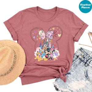 a pink t-shirt with a Disney-themed graphic, a straw hat, denim shorts, and sunglasses.