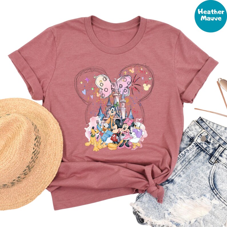 a pink t-shirt with a Disney-themed graphic, a straw hat, denim shorts, and sunglasses.