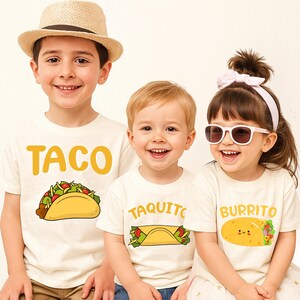 May include: Three children wearing off-white t-shirts with food-themed graphics. One shirt says "TACO" with a taco illustration, another says "TAQUITO", and the third says "BURRITO" with a smiling burrito. One child wears a straw hat.
