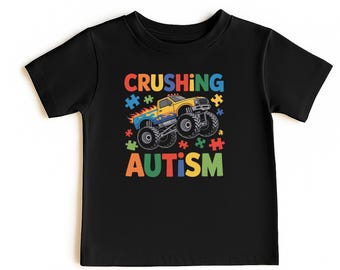 May include: Black t-shirt featuring a colorful graphic of a monster truck crushing puzzle pieces. The text reads "Crushing Autism" in bright, bold letters. The design includes a yellow and blue monster truck.