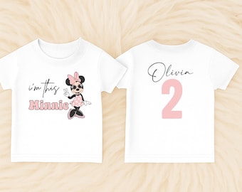 May include: A white short-sleeved t-shirt featuring a graphic of Minnie Mouse wearing sunglasses and a pink polka dot dress with the text i'm this Minnie. The back of the shirt displays the name Olivia in script and the large pink number 2.